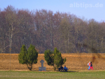 Wegkreuz unter Bäumen mit Bank